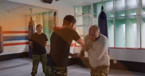 Men practicing wrist control and grappling techniques in camouflage combat training gym