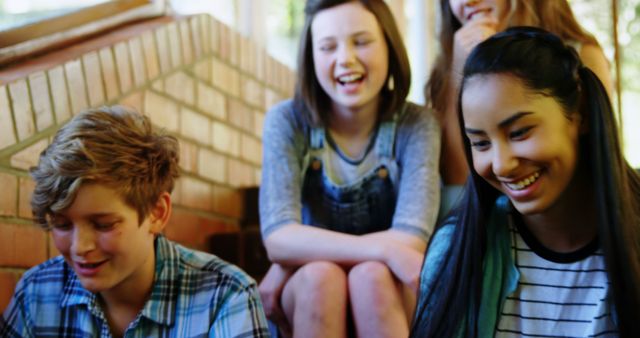 Showing diverse teenagers enjoying a sunny day and laughing together on outdoor steps. This can be used to depict themes of youth, friendship, happiness, inclusion, and outdoor activities. This image is ideal for educational materials, social media content, and advertisements targeting teenagers or promoting unity and diversity.