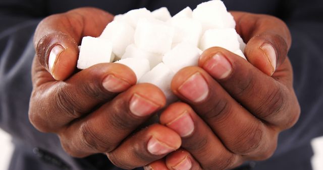 African American hands are cupped together, holding a pile of sugar cubes, with copy space. The image draws attention to dietary choices and may symbolize the discussion around sugar consumption and health.