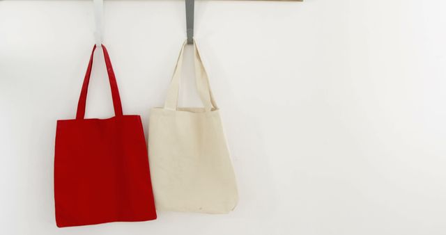 Two tote bags, one red and one beige, hang against a white background, with copy space - Download Free Stock Photos Pikwizard.com