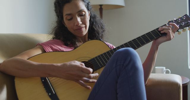 Happy biracial woman sitting on the sofa playing with guitar. domestic life and leisure time concept.