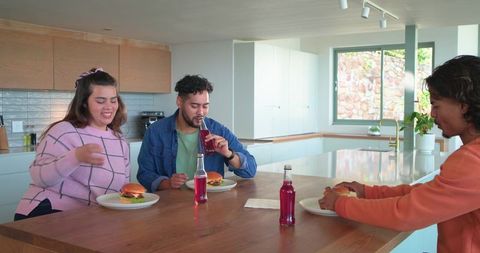Friends sharing burgers at modern kitchen island enjoying casual meal and bottled drinks