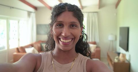 African american woman smiling taking selfie in sunlit living room with gold necklace