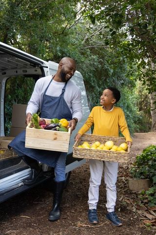 African american father and son unloading fresh produce from van on wooded country lane