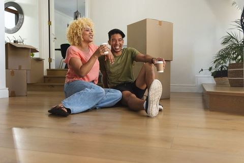 Multicultural couple sitting on floor unpacking boxes and sipping coffee in new home