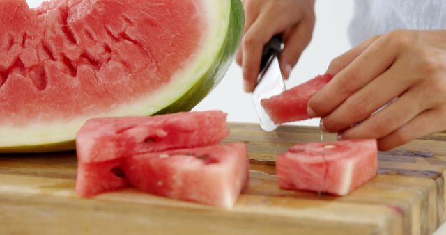 A person is slicing a ripe watermelon on a wooden cutting board, with copy space. Fresh watermelon being cut is a common preparation for a refreshing summer treat.