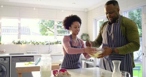 Couple Whisking Batter Together in Bright Modern Kitchen Wearing Striped Aprons