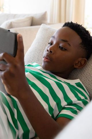African american preteen boy reclining on couch holding smartphone watching screen