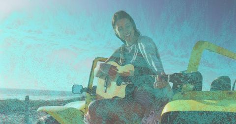 Strumming woman playing acoustic guitar on yellow dune buggy at sandy shoreline ocean view