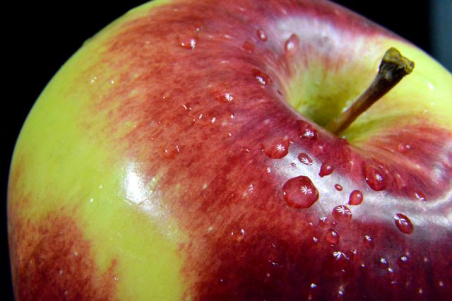 This image captures a detailed close-up of a fresh apple with vibrant red and yellow colors, adorned with water droplets, showcasing its freshness and juiciness. Ideal for use in health and nutrition articles, food blogs, and websites promoting healthy eating. Perfect for advertisements of organic produce and healthy lifestyle materials.