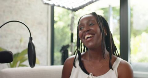 Woman laughing while speaking into microphone during relaxed living room podcast recording