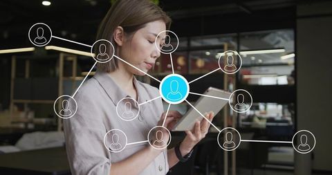 Woman holding tablet checking digital network connections in modern open-plan office