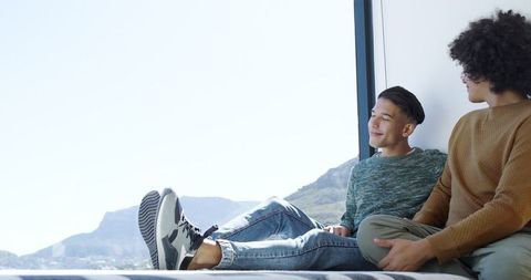 Male Friends Relaxing by Picture Window With Mountain View