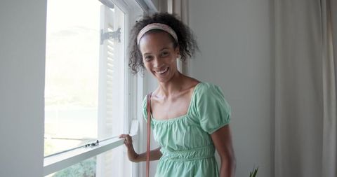Smiling Woman in Light Green Dress by Window Embracing Sunlight