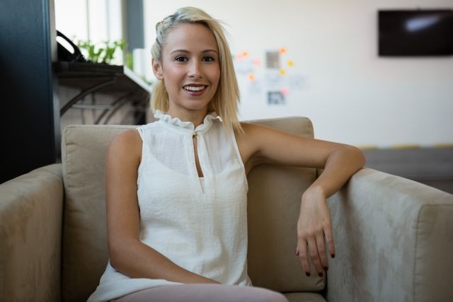 Portrait of smiling young Caucasian blonde businesswoman sitting on sofa at office. She is smiling and looking at camera
