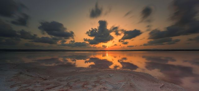 Landscape showing a stunning sunrise over salt flats with dramatic clouds reflected on calm water. Ideal for use in travel, nature, and landscape projects to evoke feelings of serenity, peacefulness, and natural beauty. Perfect for backgrounds, wallpapers, and print materials emphasizing calm and inspiring landscapes.