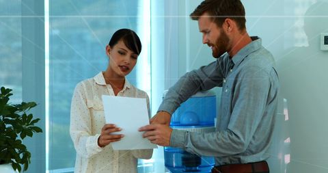 Colleagues discussing documents near office water cooler