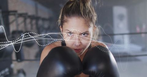 Woman boxer holding guard with black gloves in boxing ring showing intense focus
