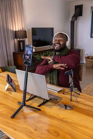 African american creator recording live stream at home with laptop, microphone, headphones
