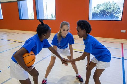 Teenage girls team huddling in school gymnasium with basketball