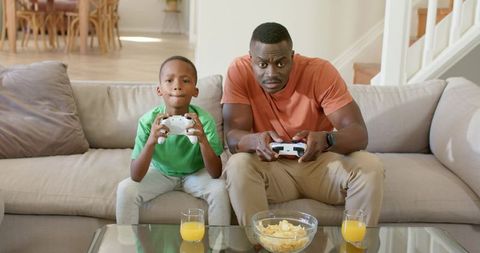 African American Father and Son Playing Video Games on Couch Sharing Cozy Family Time