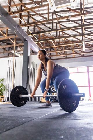 Asian woman performing deadlift with olympic barbell in bright industrial gym