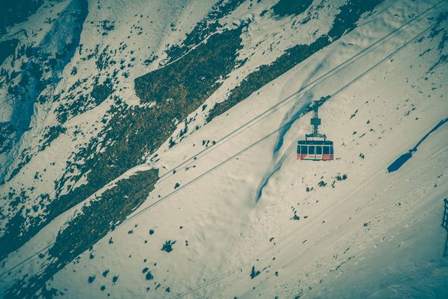 Red cable car ascending a snowy mountain, showing rugged terrain. Ideal for travel and tourism promotion, winter sports advertising, skiing destination marketing materials, or transportation-themed content.
