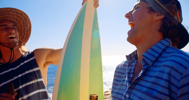 Two friends enjoying a sunny day at the beach, laughing and holding the surfboard while having drinks. Ideal for marketing summer vacations, beach holidays, and friendship-themed projects.