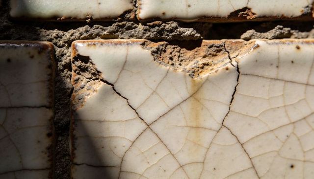 Weathered glazed ceramic tile revealing craquelure and chipped edge with mortar shadow