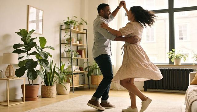 Couple twirling in sunlit living room, casual home dance among indoor plants