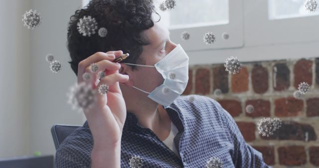 This visual juxtaposes a man wearing a face mask in an office with digital representations of COVID-19 virus particles. Ideal for safety campaigns, educational materials on virus transmission, measures for preventing viruses in workplaces, or news articles on workplaces adapting to COVID-19.