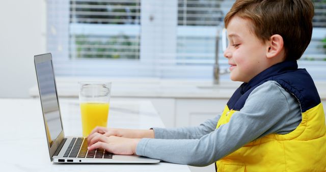 Boy wearing yellow jacket using laptop for online learning at home. Smiling child typing on keyboard. Useful for education, online classes, technology, e-learning materials, homeschooling guides.