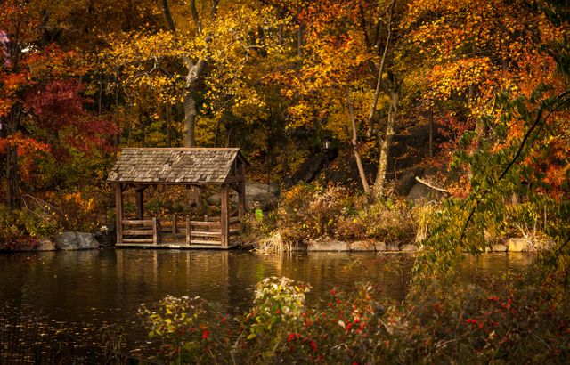 Rustic wooden boathouse on a tranquil lake surrounded by vibrant autumn foliage. Ideal for designs needing a calm, scenic, and seasonal atmosphere. Perfect for articles about fall travel destinations, relaxation, nature, and landscape photography.