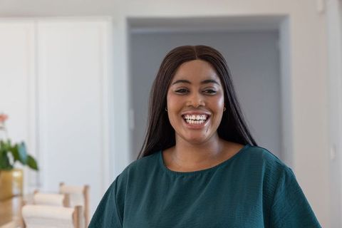African american woman smiling in contemporary kitchen wearing teal top, natural light