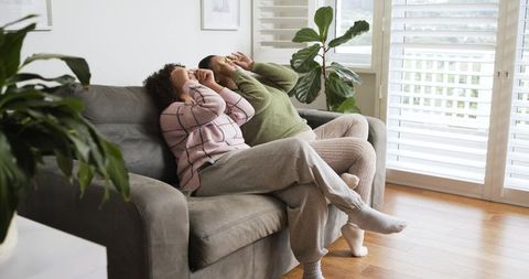 Two women laughing and covering faces on gray sofa in bright cozy living room