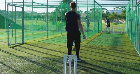 Cricket coach guiding batsman in outdoor nets practice on artificial turf at sunset