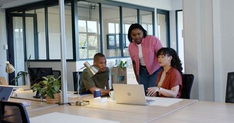 Diverse team collaborating around laptop in modern open-plan office with natural light