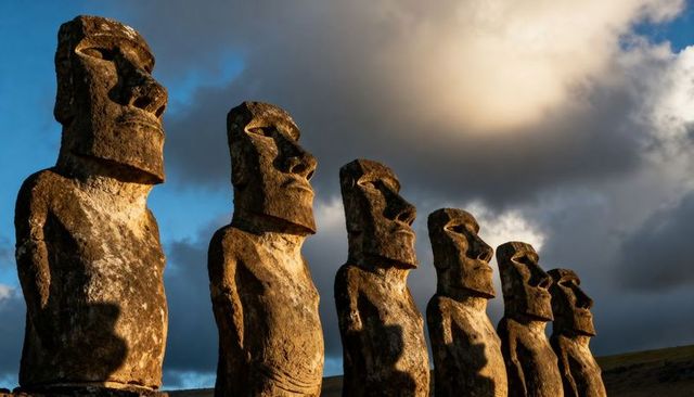 Moai statues standing in row on rapa nui ahu casting long shadows at golden hour