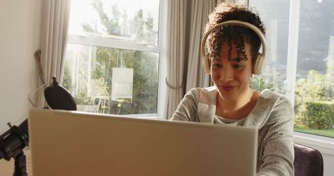 African American woman recording podcast from sunlit home office wearing headphones
