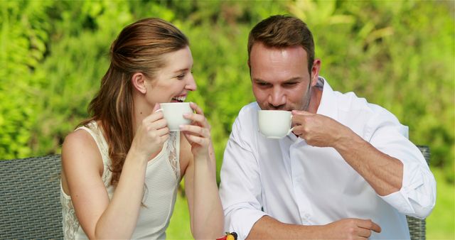 Couple enjoying coffee together outdoors in a sunny garden. Ideal for content about relationships, leisure, coffee culture, outdoor relaxation, and lifestyle. Great for websites, advertisements, blogs, and social media posts aimed at promoting happiness, quality time, and outdoor activities.