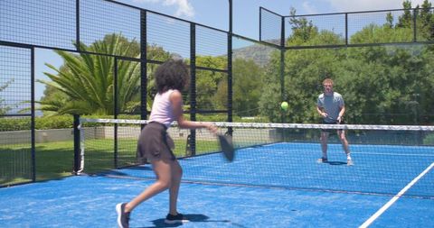 Players playing padel on blue court, swinging paddle and returning ball in sunny match
