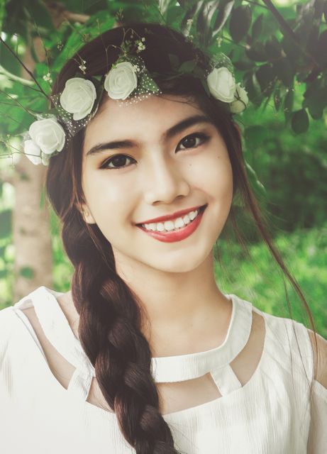 A young woman with a braided hairstyle and a flower crown is smiling in a natural outdoor setting. Perfect for use in beauty and lifestyle magazines, nature-themed advertisements, or social media campaigns focusing on happiness and beauty.