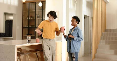 Young couple making morning coffee at modern kitchen island, man reaching for mug