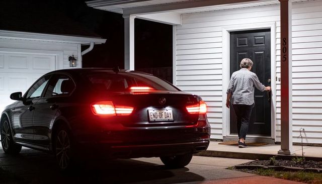 Senior woman returning home at night with dark sedan taillights lit and 'end-of-day' plate