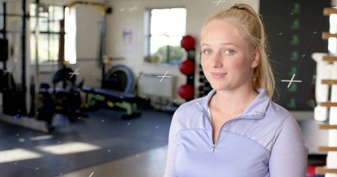 Young Woman Standing in Sunlit Gym Wearing Light Purple Zip-Up Top