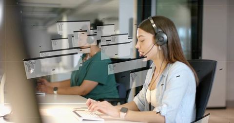 Indian woman speaking and typing with headset at call center desk with glass partitions