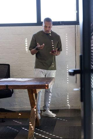 African american man standing in urban office holding smartphone, professional in daylight
