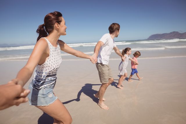 Family holding hands at beach during sunny day