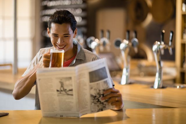 Smiling man having beer while reading newspaper in a restaurant