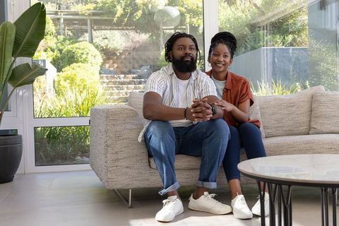 Couple relaxing on sofa in bright modern living room with garden view and glass walls